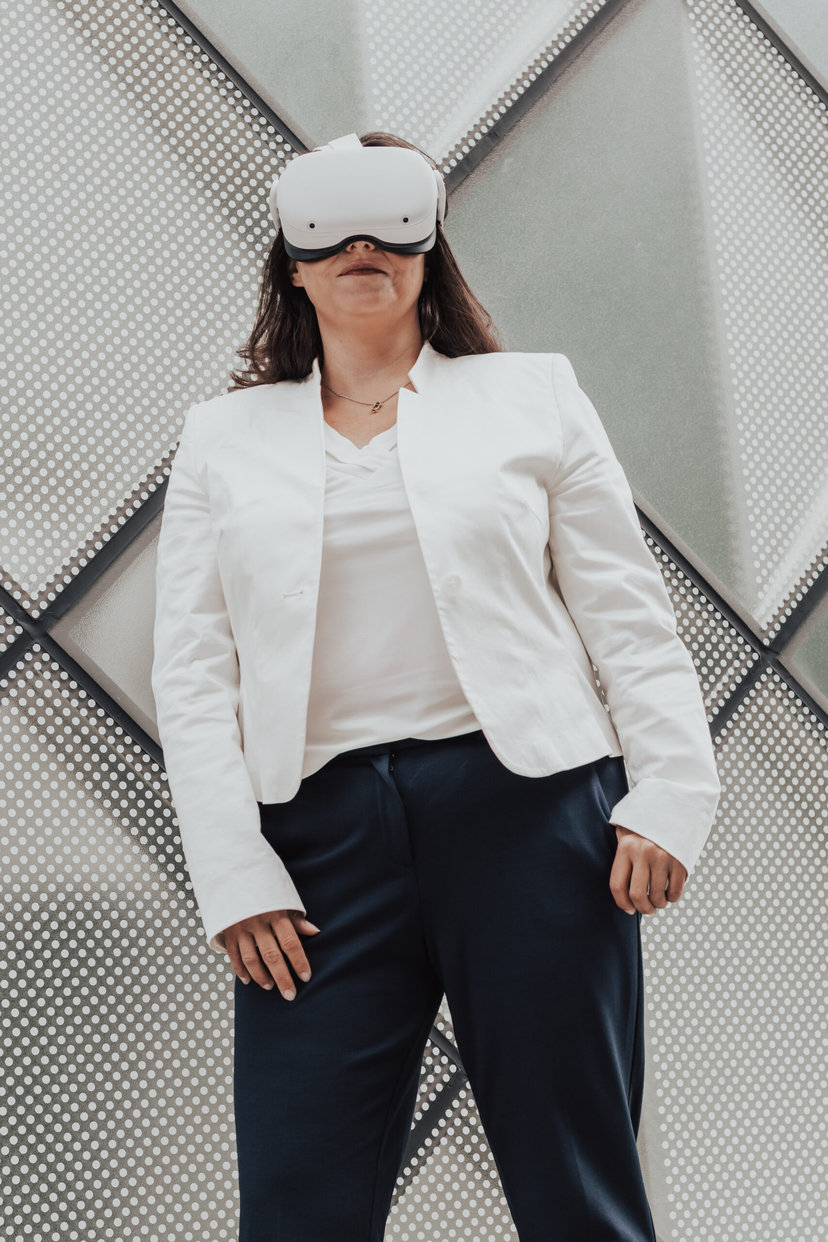 Das Bild zeigt Prof. Dr. Ellena Werning mit einer Virtual Reality Brille vor einer futuristischen Wand. Sie scheint durch die Brille in die Zukunft zu blicken. Das Bild symbolisiert die Zukunft, die durch die Nutzung von Virtual Reality klarer sichtbar wird.